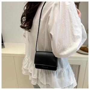 Detail shot of a black minimalist leather crossbody bag with metallic bar decoration