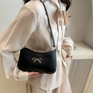 Vintage black baguette shoulder bag with a gold bow buckle worn by a model in soft light