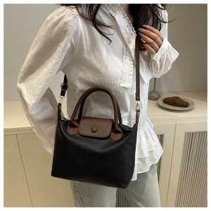 Detail of black pebbled leather tote bag with brown contrast handles and buckle flap