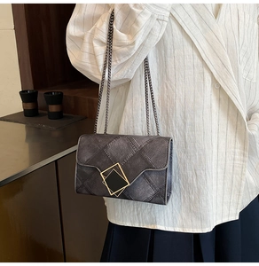 Detail of grey denim crossbody bag with gold buckle and chain strap on a model
