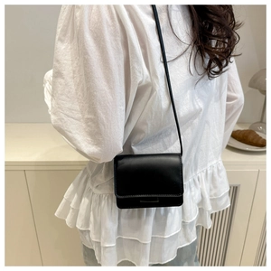 Minimalist black leather crossbody bag with flap cover shown on model with shoulder strap