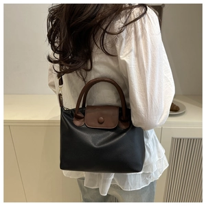 Detail of a two-tone black and brown leather pillow bag worn by a model in a home setting