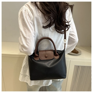 Detail of black pebbled leather pillow bag with brown straps and circular buckle