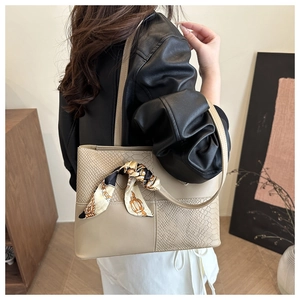 Detail of beige tote bag with snakeskin texture and decorative silk scarf on the handle