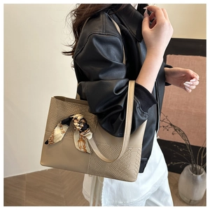Detail of beige tote bag featuring snakeskin pattern and silk scarf handle decor