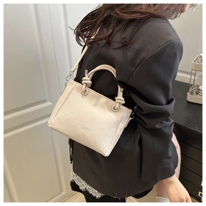 Detail of a chic cream leather crossbody bag with unique knot handle and logo