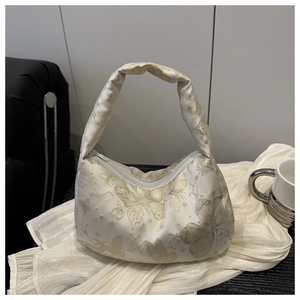 Detail of cream fabric handbag featuring golden butterfly embroidery and star patterns