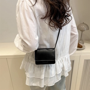 Minimalist black leather square crossbody bag styled with a white ruffle shirt for women