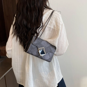 Sac bandoulière gris matelassé avec chaîne et boucle géométrique porté par un mannequin