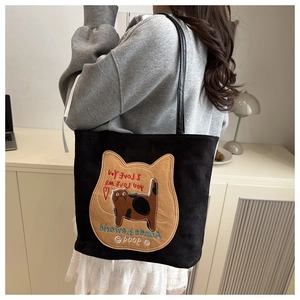 Close-up of black canvas tote bag with yellow cat embroidery patch in a home setting