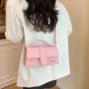 Petit sac carré rétro rose avec logo doré porté par un mannequin en blazer blanc