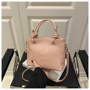 Detail showing the light pink lychee texture leather bag with a unique knotted handle design