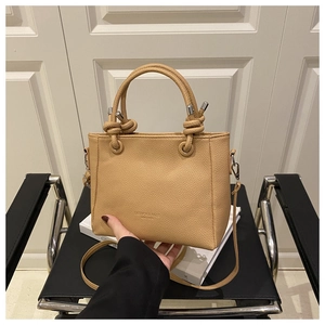 Close-up of khaki textured leather bag featuring a knotted handle and metal hardware hooks