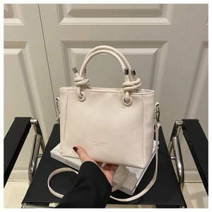 Close-up of cream square crossbody bag with unique knot handle and textured leather finish