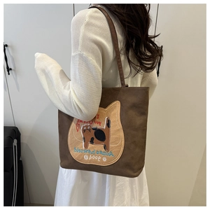 Detail of canvas tote bag with embroidered cat patch and brown shoulder straps