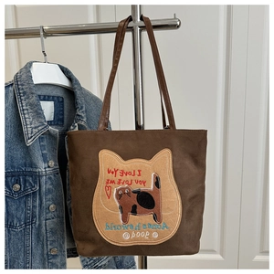 Detailed close-up of dark brown suede tote bag with embroidered cat and heart patch
