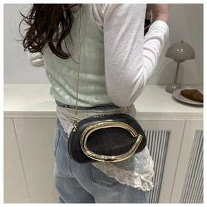 Detail of a black leather crossbody bag with a large gold oval buckle and chain strap