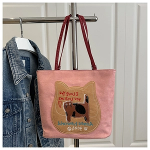 Pink cat-themed tote bag detail showing embroidery and deep red handles on canvas fabric