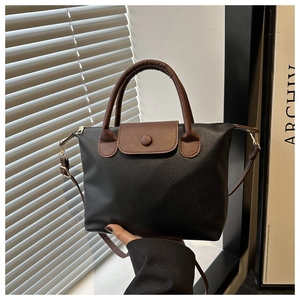Close-up of black lychee grain leather pillow bag with brown handle and metal zipper detail