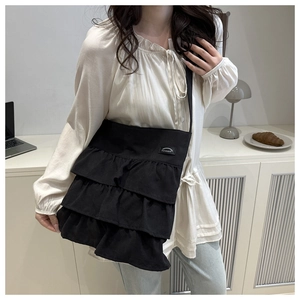 Detail of black tiered ruffle shoulder bag with small woven label in cozy home setting