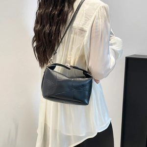 Minimalist black leather handbag with geometric patterns worn by a model on shoulder