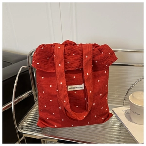 Gros plan du sac cabas rouge gaufré à motif floral blanc et écusson de la marque