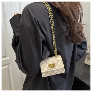 Close-up of cream crossbody bag with brown M-pattern and gold chain strap on shoulder