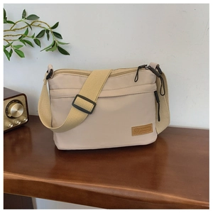 Dettaglio della borsa a tracolla in tela bianco sporco con logo in pelle e zip