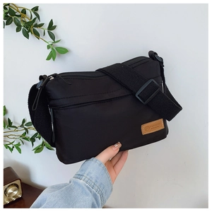 Dettaglio borsa a tracolla in nylon nero con tasche a zip e toppa in pelle marrone
