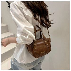 Detail view of retro brown bucket bag with gold lettering and rivet accents on a model