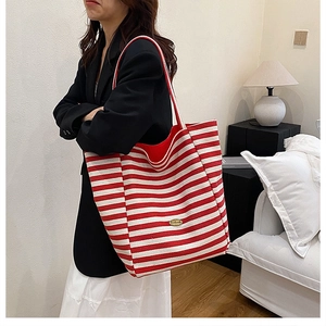 Close-up of a red and white striped canvas tote bag with metal logo in a home setting