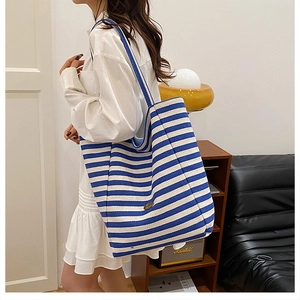 Detail of blue and white striped canvas tote bag worn by a model in a minimal room