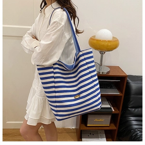 Detailed view of a blue and white striped canvas tote bag styled on a female model