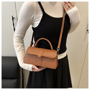 Close-up of brown textured crossbody bag with triangular buckle and quilted detailing