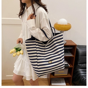 Detail of blue striped canvas tote bag with gold metal logo plaque and large capacity