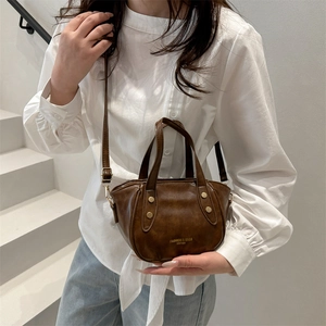 Deep brown bucket bag with gold hardware and top handles shown on model in sunlight