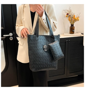 Detail of black tote bag set with embossed skull pattern and metallic skull buckle