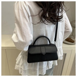 Model view of black square crossbody bag with triangular flap detail in home setting