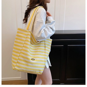 Detail of yellow striped canvas tote bag with contrast shoulder strap and brand label