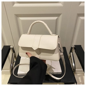 Detail view of cream white square crossbody bag with top handle on a black chair