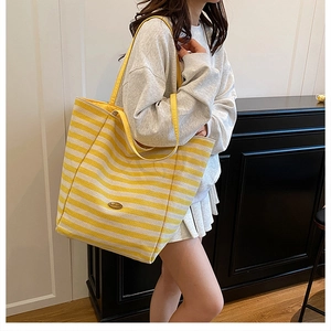 Side view of a large yellow and white striped canvas tote bag worn by a model