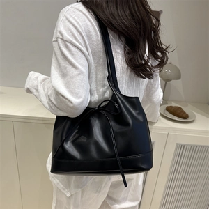 Minimalist black faux leather tote bag with stylish bow detail shown on a shoulder