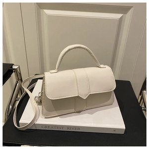 Close-up of cream square crossbody bag with rounded handle on minimalist white books