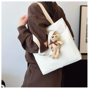Detail of white canvas tote bag with shoulder strap and cute plush bear charm