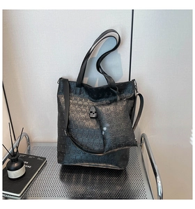 Detail of grey tote bag featuring skull embossed pattern and metallic skull ornament