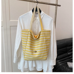 Detail of yellow and white striped tote bag with wide strap and oval metal brand tag