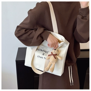 Detailed shot of white canvas tote bag with wide strap and cute plush bear charm accessory