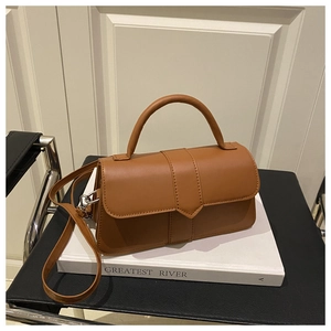 Detail of a brown leather handbag with top handle and strap on a book background