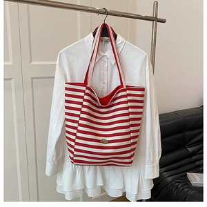 Detail view of large red and white striped canvas tote bag with gold metal plate
