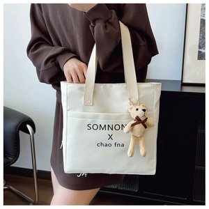 Detail of white square tote bag with logo print and cute knitted bear charm on shoulder